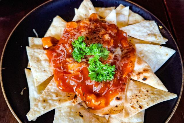 Plate of nachos topped with melted cheese, tomato sauce, grated cheese and parsley, surrounded by crisp tortilla chips.