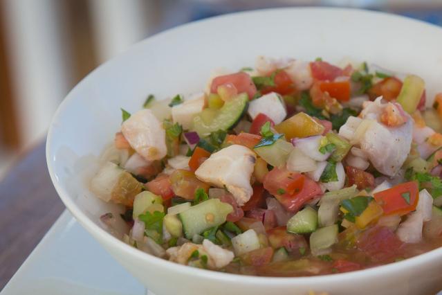 A bowl of raw fish salad with pieces of fish, tomato, cucumber, red onion, and herbs mixed together.
