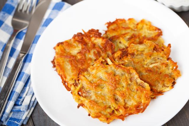 Golden oven-baked potato cakes on a white plate beside a knife, fork and blue checked cloth.