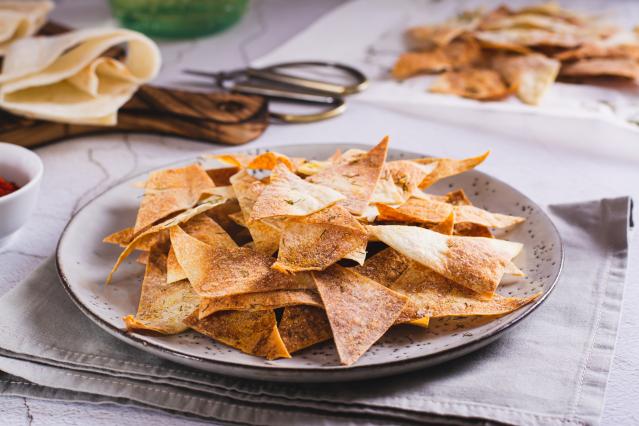 Plate of oven-baked tortilla chips seasoned with spices, served on a grey plate with extra tortilla pieces in the background.