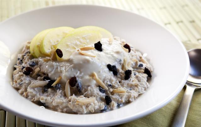 A bowl of overnight porridge topped with yoghurt, apple slices, dried fruit and flaked almonds, with a spoon beside the bowl.