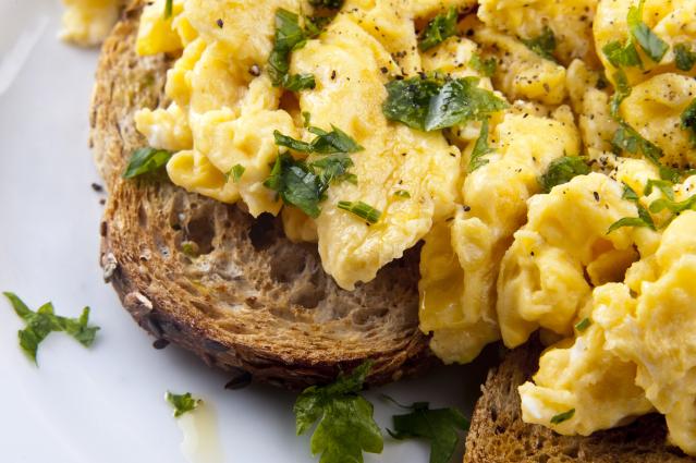 Creamy scrambled eggs on toasted grain bread, topped with chopped parsley and black pepper.