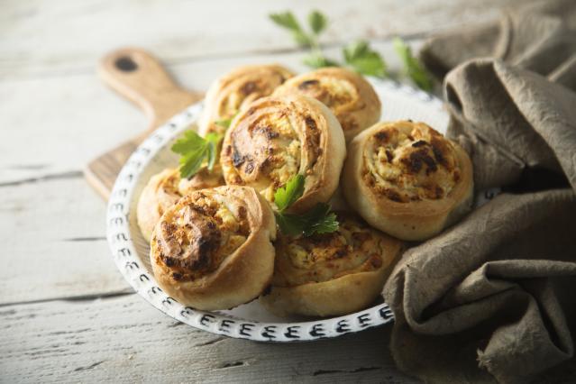 A plate of baked savoury pinwheels with golden pastry and a cheesy filling, garnished with parsley.
