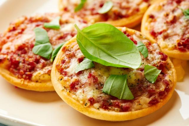 Small pita bread pizzas topped with melted cheese, tomato sauce and fresh basil leaves on a plate.