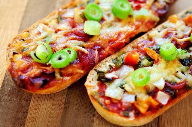 Pizza-topped bread rolls with melted cheese, tomato sauce, vegetables and sliced spring onion on a wooden board.