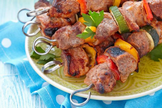Grilled pork kebabs with pieces of zucchini and red and yellow capsicum on skewers, served on a plate.