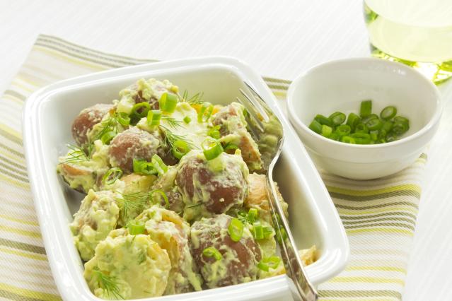 A bowl of potato salad with creamy avocado dressing, topped with sliced spring onion and fresh herbs.