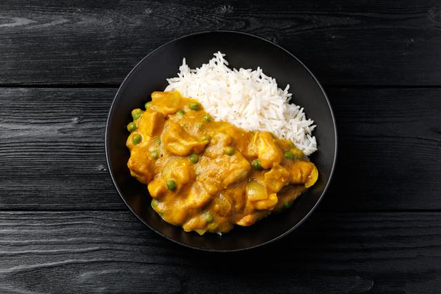 Bowl of pumpkin and chicken curry with peas, served with white rice on a dark wooden table.