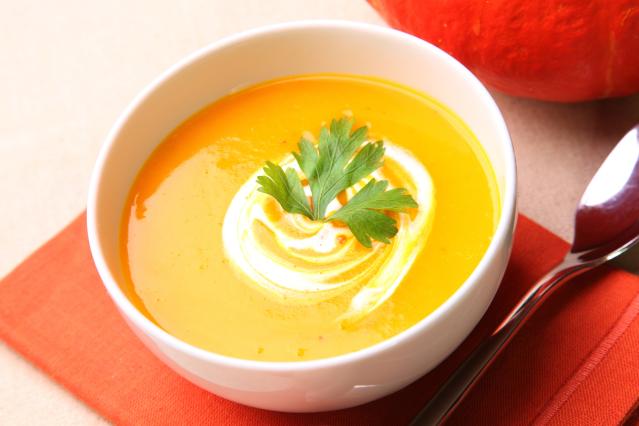 A bowl of smooth pumpkin and kūmara soup topped with a swirl of cream and a parsley leaf.