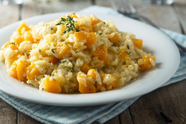 A plate of creamy pumpkin risotto topped with herbs and grated cheese.