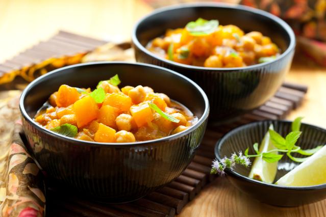 Two bowls of pumpkin and chickpea curry garnished with fresh herbs, served on a wooden table.