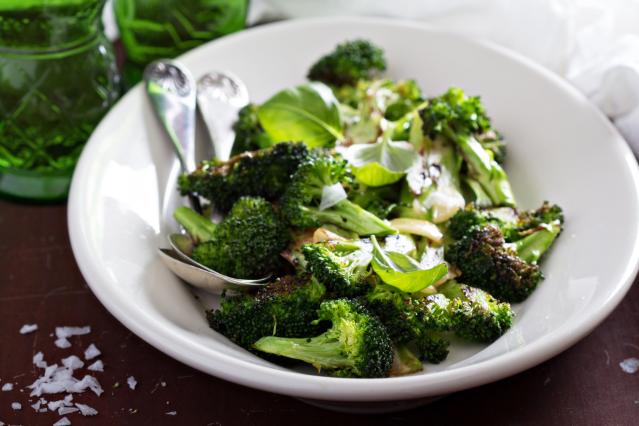 Bowl of roasted broccoli with fresh basil leaves, served with spoons.