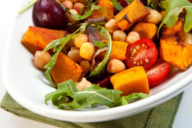 A bowl of roasted vegetables and chickpeas including kūmara, beetroot, cherry tomatoes, and rocket leaves.