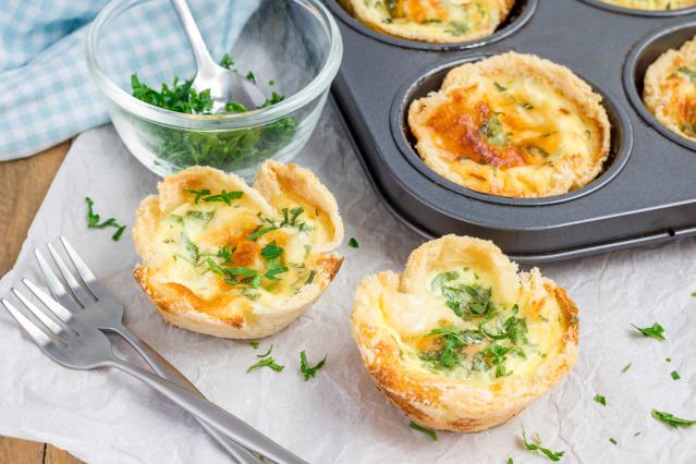 Savoury bread cases filled with egg, cheese, and vegetables, baked in a muffin tray and garnished with herbs.