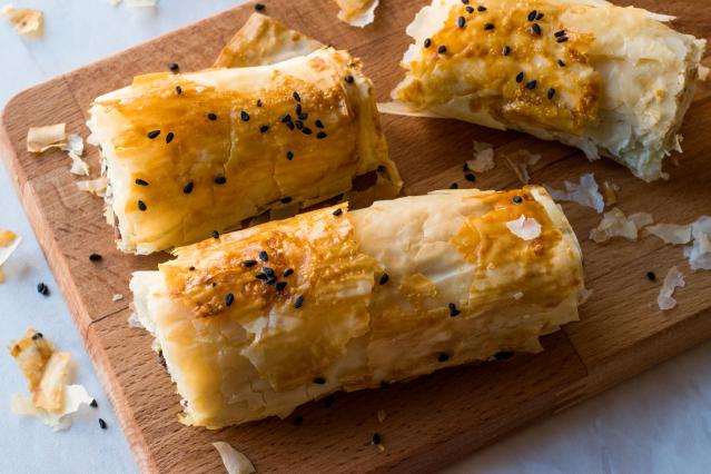 Crispy savoury filo rolls sprinkled with black sesame seeds on a wooden board.