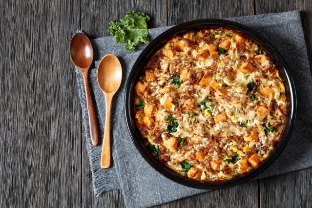 Baked savoury vegetable and mince dish in a round baking dish, topped with kumara, greens, and melted cheese.