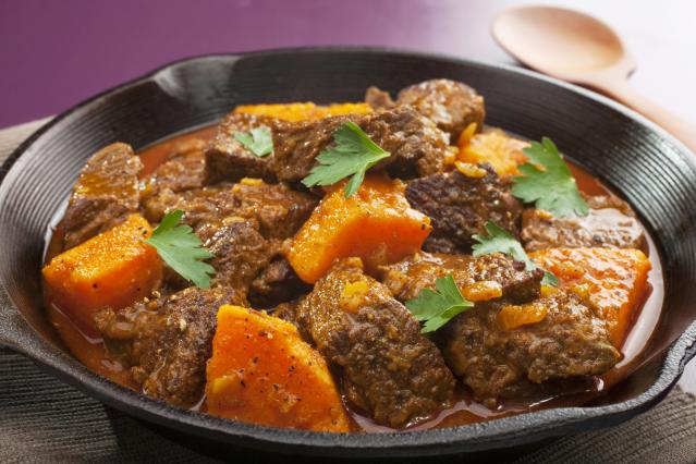 A bowl of slow-cooked beef curry with kūmara chunks in a rich red sauce, garnished with parsley leaves.