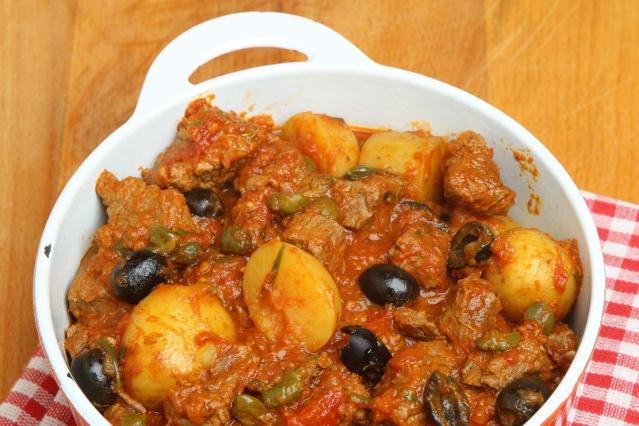 A bowl of slow-cooked beef stew with potatoes, olives, and capers in a rich tomato sauce.