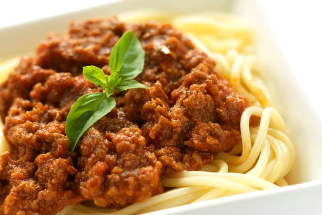 Spaghetti topped with rich meat bolognese sauce and garnished with fresh basil leaves.