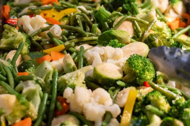 Close-up of mixed cooked vegetables including broccoli, cauliflower, green beans, carrots, and capsicum.