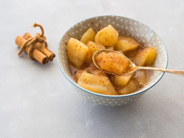 A bowl of stewed fruit sprinkled with cinnamon, with a spoon lifting a piece of fruit from the bowl.