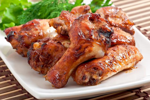 A plate of cooked chicken drumsticks and wings with a glossy glaze, served with leafy greens in the background.