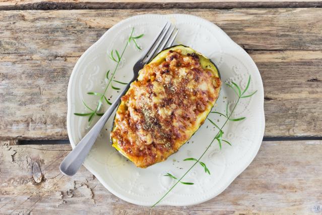 Baked stuffed kamo kamo topped with melted cheese on a white plate with a fork.