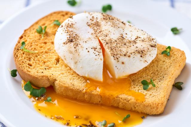 A soft poached egg with runny yolk on toasted bread, sprinkled with black pepper and small green herbs.