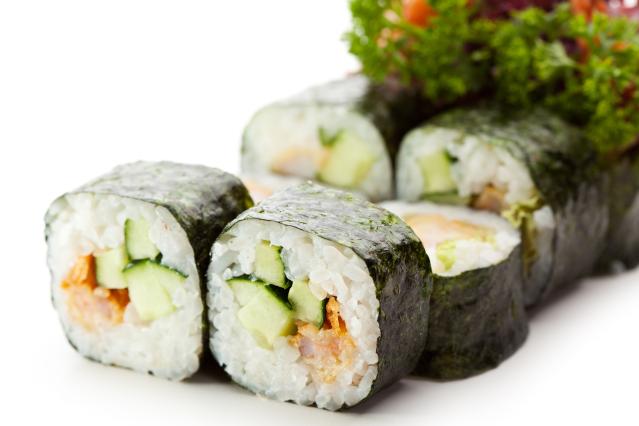 Sushi rolls wrapped in seaweed and filled with rice, cucumber, and tuna, served with leafy salad greens in the background.