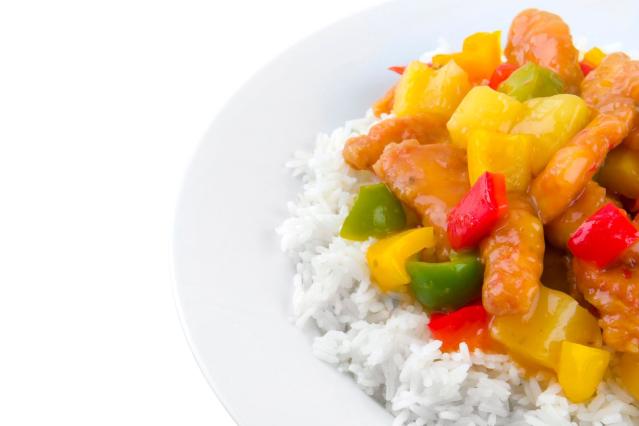 Sweet and sour chicken with pineapple and red, green, and yellow capsicum served on white rice.