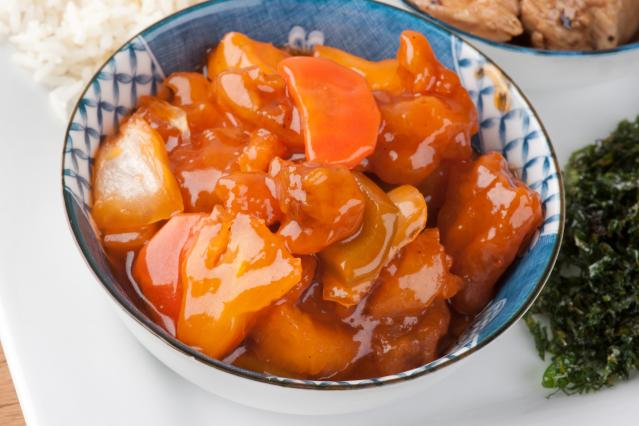 A bowl of sweet and sour pork with pineapple, onion, and carrot pieces in a glossy orange sauce.