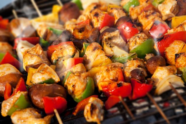 Barbecue skewers cooking on a grill with pieces of chicken, capsicum, onion, and mushrooms.
