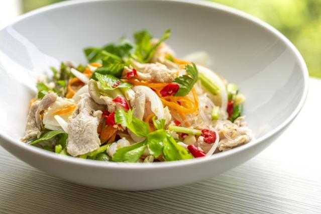 Bowl of Thai chicken salad with noodles, vegetables, herbs and sliced chilli.