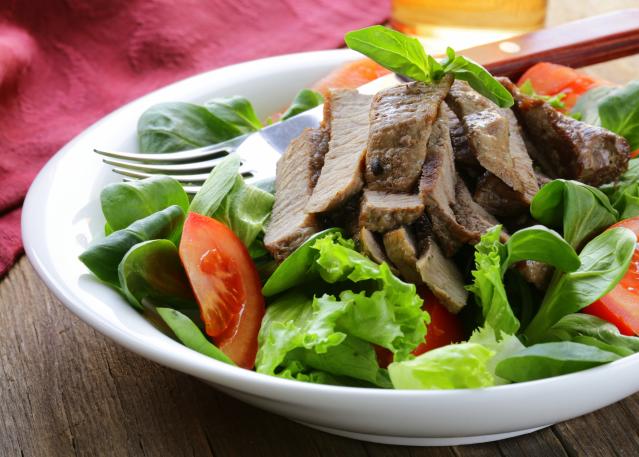Salad with sliced beef, lettuce leaves, and tomato wedges served in a white bowl.