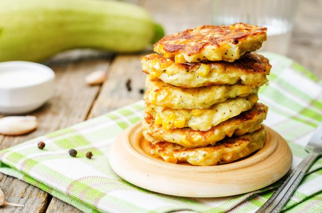 Stack of golden corn fritters on a wooden plate with corn kernels visible throughout the fritters.