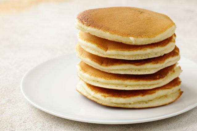 Stack of five plain golden pancakes on a white plate.