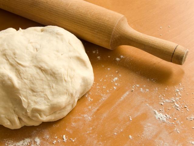 Ball of pizza dough on a floured wooden bench beside a wooden rolling pin.