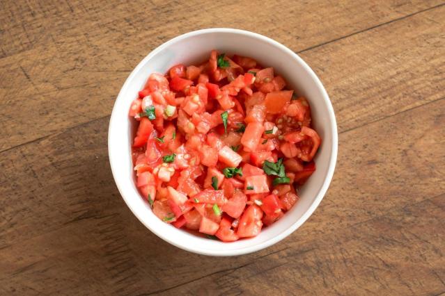 Small bowl of chopped tomato salsa on a wooden table.