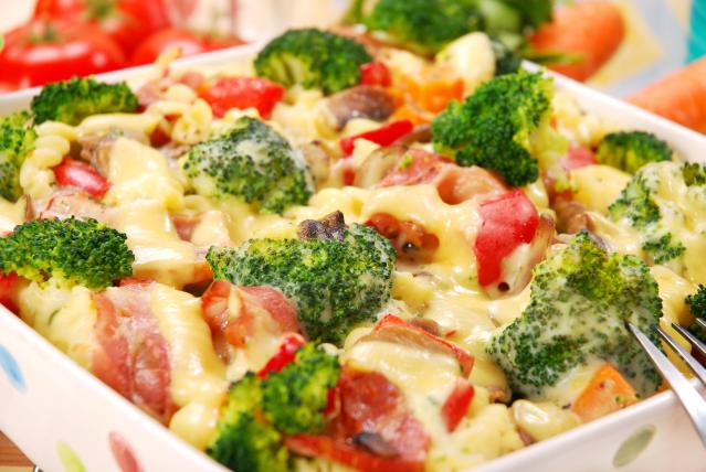 Pasta bake with broccoli, bacon, tomato, mushrooms and melted cheese in a baking dish.