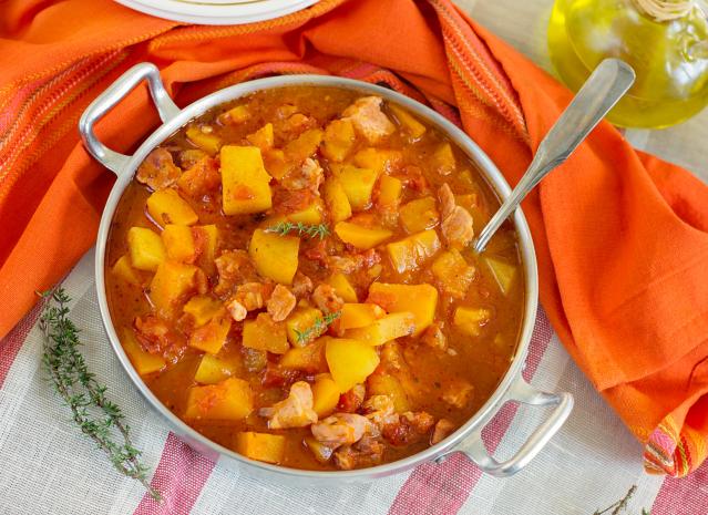 Bowl of pork stew with kūmara, pumpkin and tomato in a rich orange sauce.