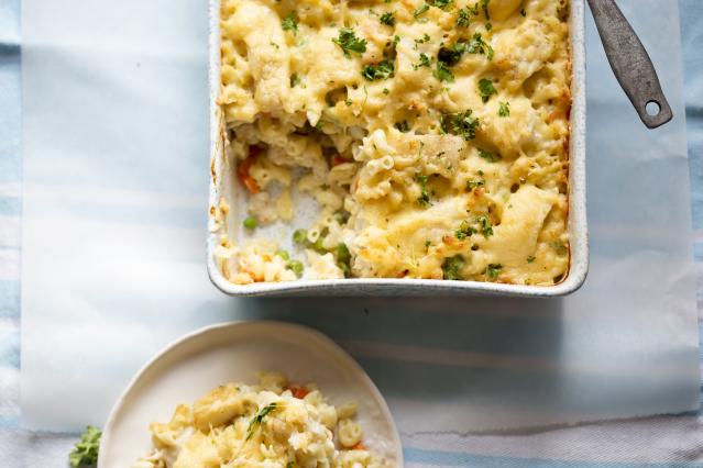 Baked tuna and cauliflower macaroni cheese in a baking dish with a serving on a plate beside it.