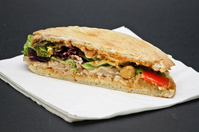 Tuna and chickpea pita pocket filled with lettuce, cucumber, red capsicum and mixed salad leaves on a white napkin.
