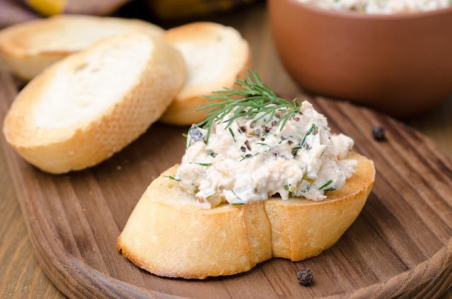 Slice of toasted bread topped with creamy tuna dip and fresh dill on a wooden board.
