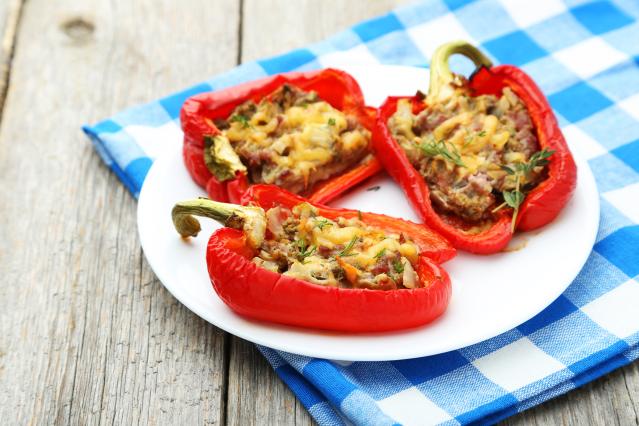 Three baked red capsicum halves stuffed with a tuna and vegetable filling, topped with melted cheese and herbs, served on a white plate.