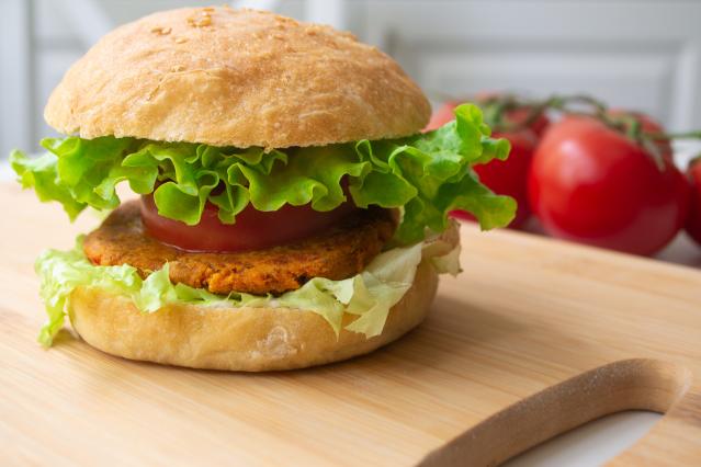 Vegetable and bean burger in a bread bun with lettuce and tomato on a wooden board.