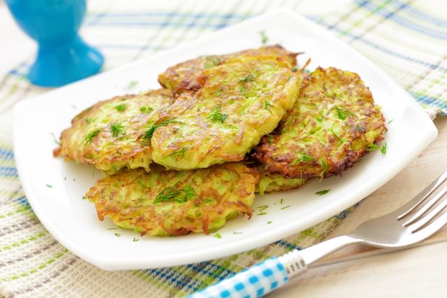 Golden vegetable and oat patties garnished with herbs on a white plate beside a fork.