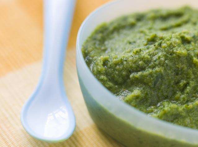 Green vegetable purée in a small bowl beside a baby spoon.