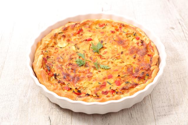 Golden vegetable quiche with visible pieces of capsicum and zucchini in a white baking dish.