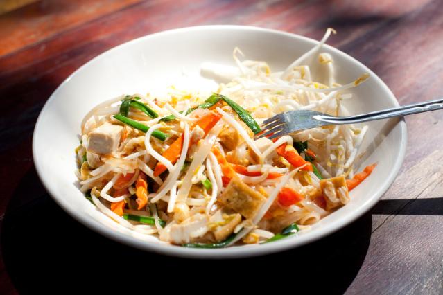 Vegetarian pad thai with noodles, tofu, bean sprouts, and vegetables served in a white bowl with a fork.