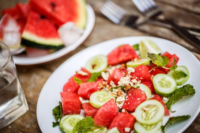 Watermelon, cucumber, and mint salad topped with chopped nuts on a white plate.